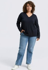 Maglione blu navy a V con maniche lunghe, realizzato in tessuto morbido, abbinato a jeans dritti azzurri chiaro e sneakers bianche. Vestibilità liscia e rilassata.