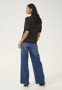 Top negro a rayas con mangas cortas, combinado con jeans azules de pierna ancha. Textura suave, ajuste casual, con bolsillos traseros y una silueta relajada.