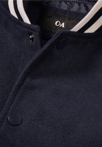 Mörkblå ulljacka med svarta tryckknappar och en ribbad krage med vita och svarta ränder, märkt C&A inuti.