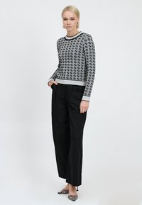 Maglione a maglia a righe bianche e nere con maniche lunghe, collo rotondo e orlo a coste, abbinato a pantaloni neri a gamba larga e tacchi decorati.