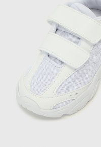 Scarpa da ginnastica bianca con tomaia in mesh e pelle sintetica, caratterizzata da due cinturini in velcro, superficie testurizzata e suola in gomma stampata.