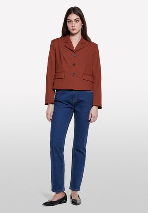 Blazer marron cropped avec col cranté, trois boutons et deux poches avant, associé à un jean droit bleu et des ballerines noires.