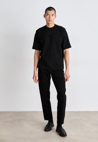 Svart bomull t-skjorte med korte ermer og rund hals, kombinert med svarte rette bukser og slip-on sko. Enkelt design, ingen mønstre.