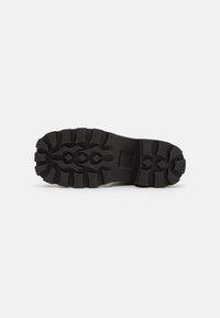 Suela de zapato de goma negra con patrones de banda de rodadura profunda, que presenta surcos hexagonales y en zigzag para una mejor agarre y tracción.