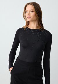 Body a maniche lunghe nero con un design aderente e decorato con piccoli cristalli sul petto. Tessuto morbido e scollatura a girocollo classica.