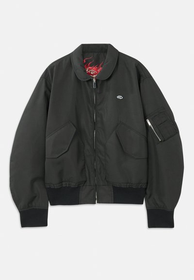 Mustmustari mustkas pusa, millel on lukuga esiosa, krae ja soonikvarrukad. Omab kahte suurt esipoolt taskut ja ühe lukuga käe tasku.