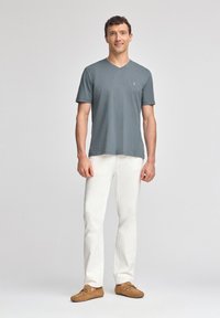 Grå t-shirt med v-ringning och korta ärmar, kombinerad med vita byxor. Outfitten har ljusbruna loafers och en minimal logotyp på t-shirten.