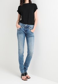 Černé tričko s krátkým rukávem v kombinaci se světle modrými skinny džínami. Má kapsy a volný střih. Doplněno černými otevřenými podpatky.