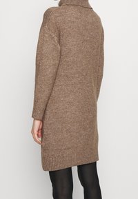 Robe pull tricotée marron avec un col montant, des poignets et un ourlet côtelés. Présente une coupe décontractée et des fentes latérales pour faciliter les mouvements.