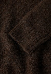 Maglione marrone lavorato a maglia che mostra un primo piano della trama del tessuto, caratterizzato da un aspetto morbido e lanuginoso con polsini a coste.