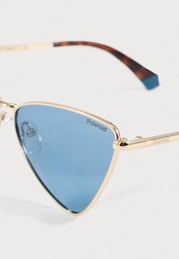 Modri trikotni leči z zlatim kovinskim okvirjem in školjkastimi nasloni za ušesa, blagovna znamka Polaroid vidna na leči in naslonu.