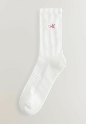 Calcetines de algodón blancos con textura acanalada y un bordado en rosa que dice "self" en el lado. De longitud media, con puntera redondeada y ajuste ceñido.