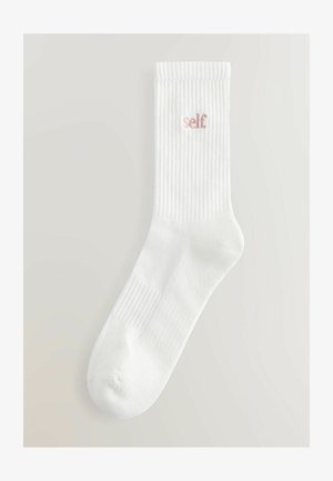 Bijele pamučne čarape s rebrastom teksturom i ružičastim vezom "self" sa strane. Srednje dužine, s zaobljenim prstima i udobnim prianjanjem.