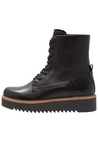 Botas de cuero negras hasta el tobillo con cierre de cordones en la parte delantera, puntera redondeada y una suela de plataforma gruesa y estriada. Presenta una media suela de color marrón claro que contrasta.