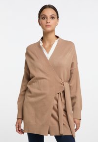 Beige wikkelcardigan gemaakt van zachte brei-stof, met een striksluiting bij de taille, geribde manchetten en een ontspannen pasvorm.