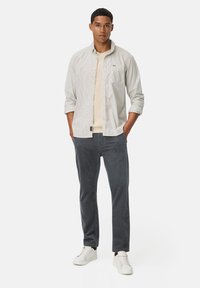 Lichtgrijs gestreefd overhemd over een beige t-shirt, gecombineerd met donkergrijze flanelle pantalon en witte sneakers. Geen opvallende patronen of accenten.