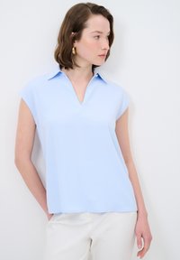 Blusa azzurro chiaro a maniche corte in tessuto leggermente strutturato, con collo a camicia e una vestibilità comoda, abbinata a pantaloni bianchi.