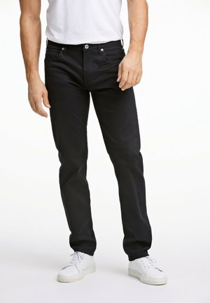 Zwarte spijkerbroek van denim met een rechte pasvorm, voorzien van een ritssluiting, vijf zakken en zilverkleurige details. Draagt met witte sneakers.
