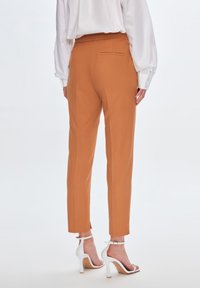 Orange tapered Hosen aus strukturiertem Stoff, mit einer Gesäßtasche, kombiniert mit weißen, geflochtenen High Heels.