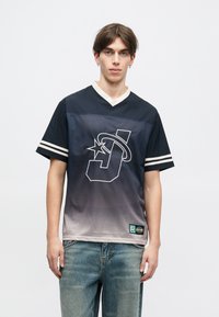 Μπλουζάκι κοντομάνικο με μπλε γκρανιέ, με μεγάλο λευκό λογότυπο που περιέχει ένα αστέρι, πλέγμα υφής και ριγωτές λεπτομέρειες στα μανίκια.