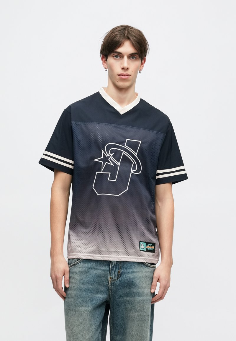 Μπλουζάκι κοντομάνικο με μπλε γκρανιέ, με μεγάλο λευκό λογότυπο που περιέχει ένα αστέρι, πλέγμα υφής και ριγωτές λεπτομέρειες στα μανίκια.