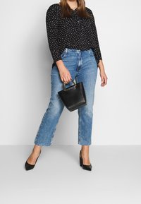 Blusa negra con lunares, jeans de tiro alto en un azul claro, zapatos de tacón negros y un pequeño bolso negro con detalles dorados.