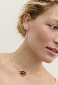 Collana choker in tonalità oro con una pietra ovale rossa, una pietra rosa più piccola e una pietra gialla, dal design minimalista.
