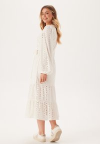 Witte oogjes jurk met lange pofmouwen, een gelaagde rok en een strik middel. Gecombineerd met lichte sneakers. Textuurstof, ademend.