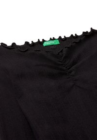 Schwarzes geripptes Oberteil mit Rüschenausschnitt und grünem "United Colors of Benetton"-Label in der Mitte.