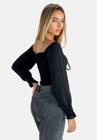 Top nero arricciato con maniche lunghe e puff, scollatura quadrata e tessuto texturizzato. Abbinato a jeans in denim grigio a vita alta.