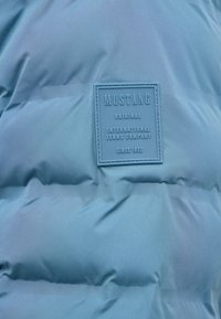 Hellblauer gepolsterter Stoff mit einem angenähten Etikett, auf dem steht: "MUSTANG Original International Jeans Company seit 1932."