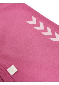 Rosa tyg med en texturerad yta som har ett vitt zick-zackmönster längs en kant. Liten varumärkesetikett med en bladdesign i hörnet.