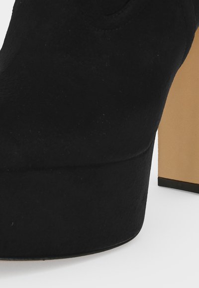 Gros plan d'une chaussure à plateforme en daim noir avec une semelle épaisse et un talon haut, massif et beige.