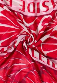 Tissu à motifs rouges et blancs torsadé en une spirale centrale, avec des lettres partielles et des formes audacieuses visibles sur le tissu.
