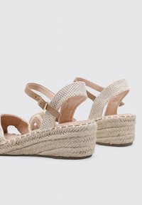 Sandalias de cuña de esparto beige con tiras de tela trenzada, hebillas ajustables en el tobillo y suela de yute trenzado.
