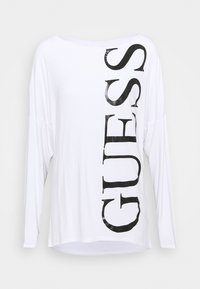 Weißes Langarmshirt mit einem glänzenden schwarzen "GUESS"-Druck, der vertikal verläuft. Weicher Stoff mit lockerer Passform und abgerundetem Saum.