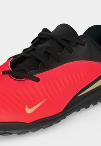 Κόκκινο και μαύρο αθλητικό παπούτσι Nike με μαύρα κορδόνια, υφασμένο πλαϊνό πάνελ και χρυσό λογότυπο Nike στην εξωτερική πλευρά.