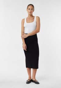 Jupe midi en tricot noir associée à un débardeur blanc. La tenue présente une silhouette ajustée, un design minimaliste et des chaussures plates noires.