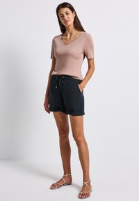 Růžové tričko s výstřihem do V, černé šortky na stažení s kapsami a stříbrné sandály na pásky. Hladká tkanina a ležérní design.