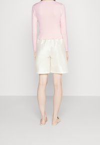 Top de manga larga rosa claro combinado con pantalones cortos de satén crema. Textura suave con ajuste holgado y un brillo sutil. Descalzo con sandalias minimalistas.