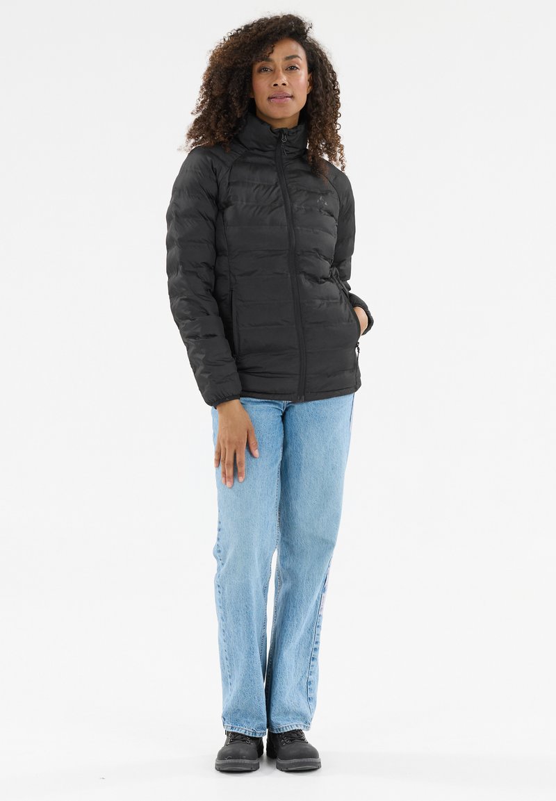 Sort dunjakke med høj krave, lodret quiltet tekstur, lynlås foran og lange ærmer, kombineret med lyseblå jeans og sorte sko.