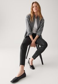 Ballerine nere dal design basso, abbinate a pantaloni scuri e a una camicia grigia con bottoni sopra una maglietta bianca. Look semplice e lineare.