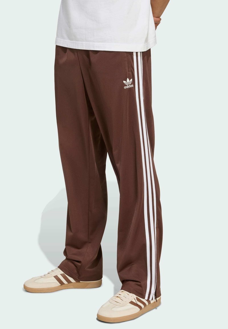 Barna sportnadrág fehér oldalsávokkal és Adidas logóval. Simább anyagból készült, laza szabású és rugalmas derékrésszel.