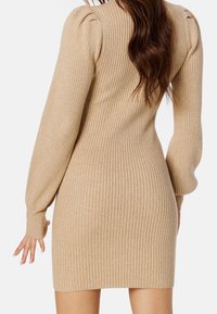Robe beige côtelée à manches longues, silhouette ajustée et détail subtil de fronces aux épaules ; texture douce, longueur mi-cuisse.