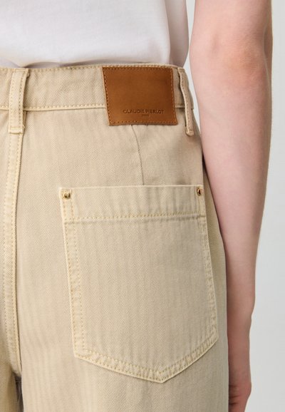 Pantalones altos de color beige con patrón de espiga, que cuentan con una etiqueta de marca de cuero en la parte posterior y un bolsillo trasero sencillo con herrajes dorados.