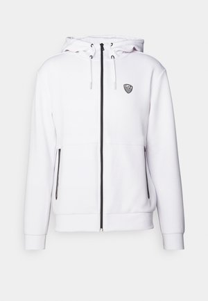 Felpa bianca con cappuccio realizzata in tessuto morbido, dotata di zip frontale, cappuccio regolabile, dettagli neri della zip e un piccolo logo sul petto.