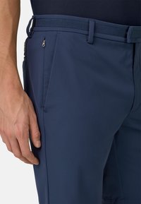 Pantaloni blu navy dal design elegante, con una tasca con zip, tessitura liscia e vita strutturata. Vestibilità sartoriale con linee pulite.