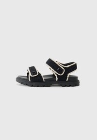 Black woven sandals with cream accents, featuring adjustable straps, a textured upper, and a rugged black rubber sole.