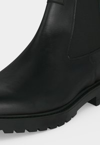 Bottine noire en cuir avec panneau latéral élastique et semelle robuste, présentée en gros plan sur un fond uni.