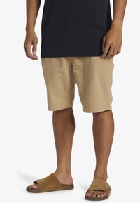 Beiga bomullsshorts med sidofar pockets, en lös passform och sydda fållar, kombinerat med bruna sandaler med halkfria remmar.